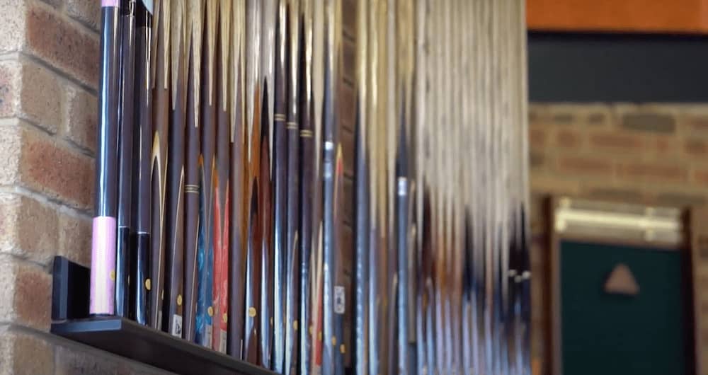 A large commercial style cue rack in the Quedos showroom displaying a huge variety of new pool cues.